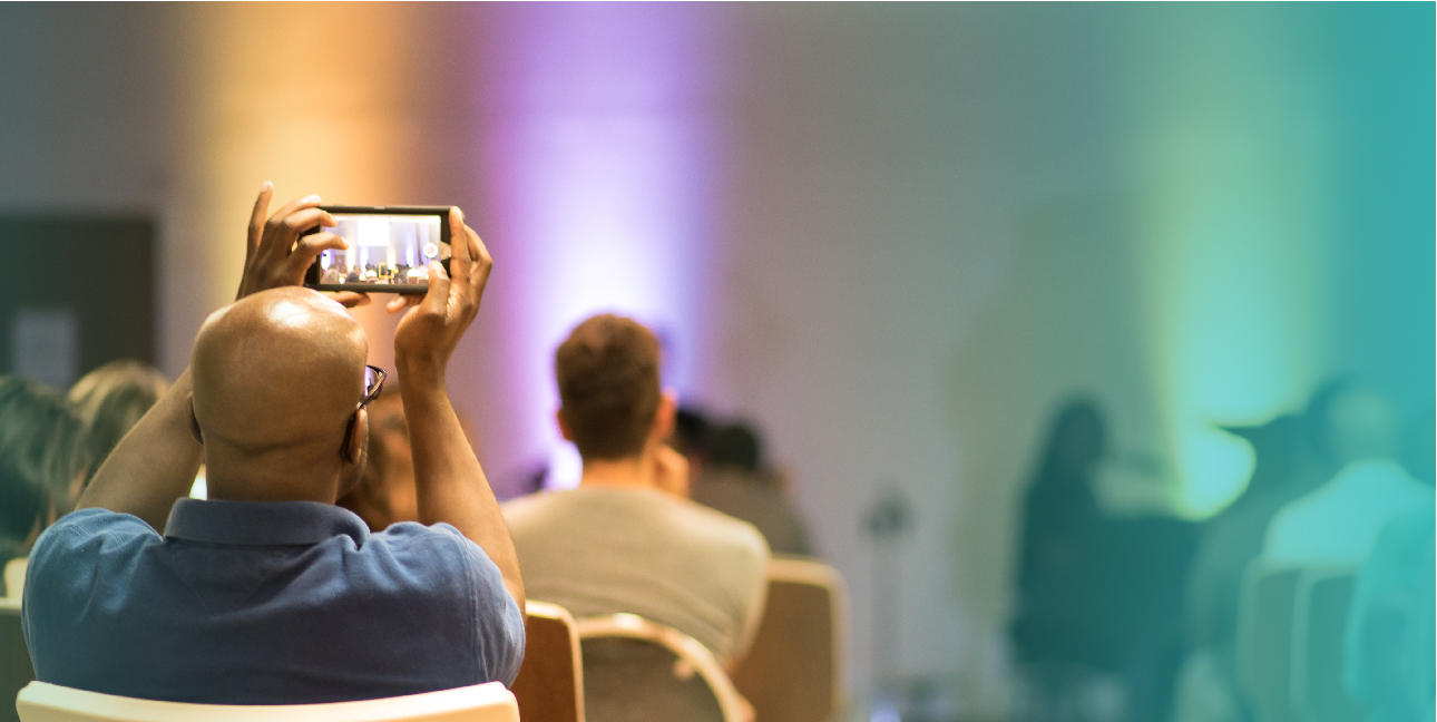 A man holds up a phone as he records a live speaking event.