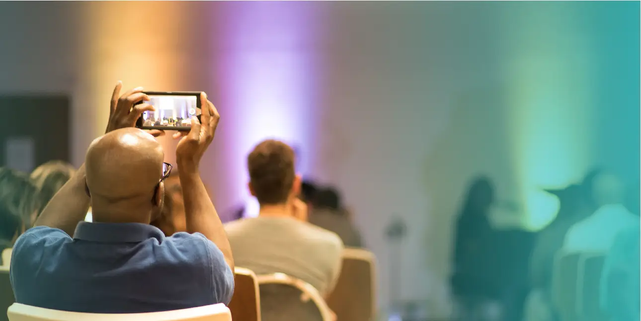 A man holds up a phone as he records a live speaking event.