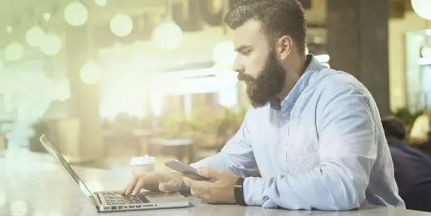 A man works on his laptop in the middle of a cafe.