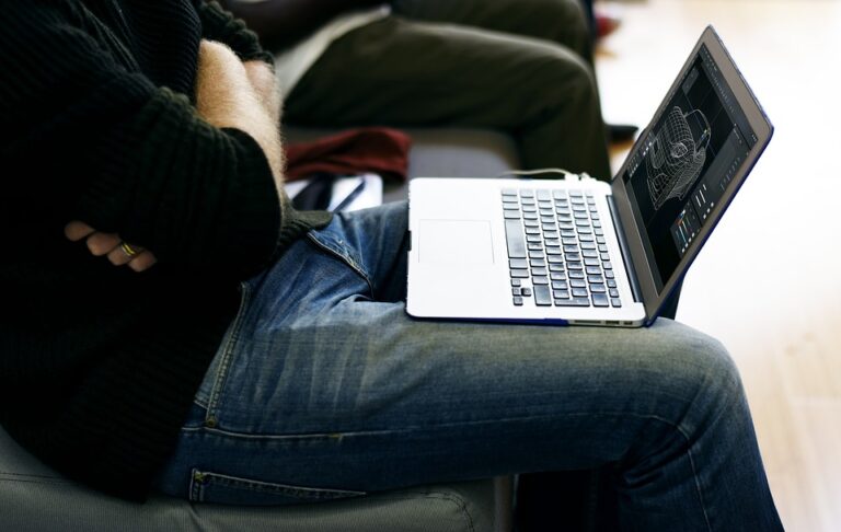 A man browses a laptop as it rests on his lap in the waiting room of an airport.