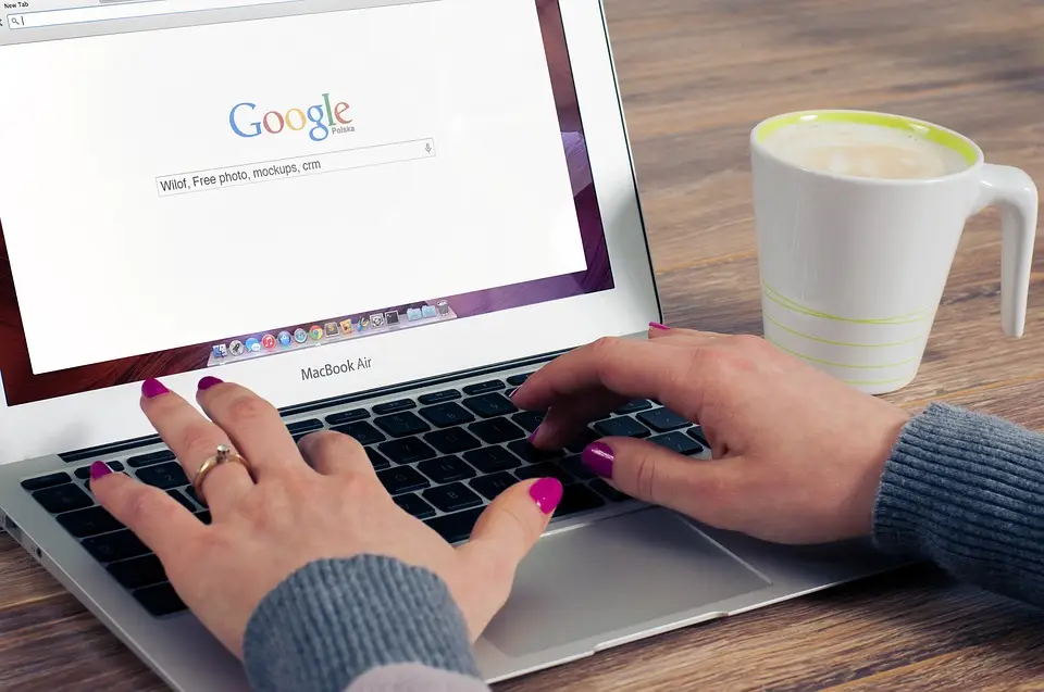 A woman browses Google on her laptop while drinking coffee.