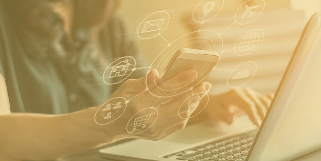 A woman holds an iPhone in front of a laptop