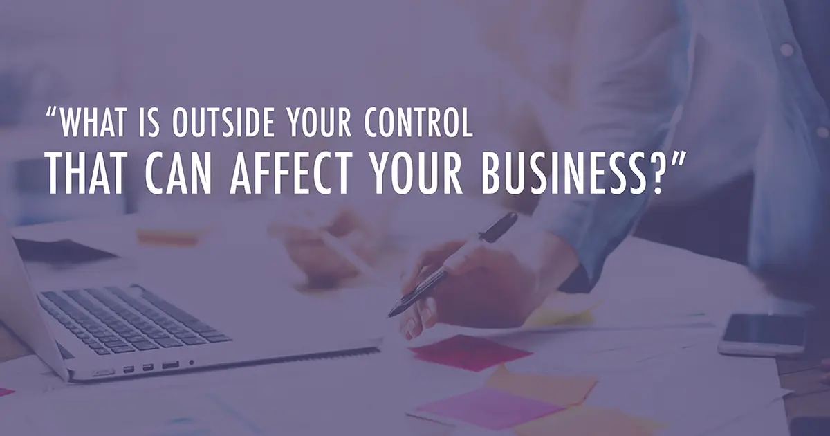 A person leans over a table covered in papers with text that reads, "What is outside your control that can affect your business?"