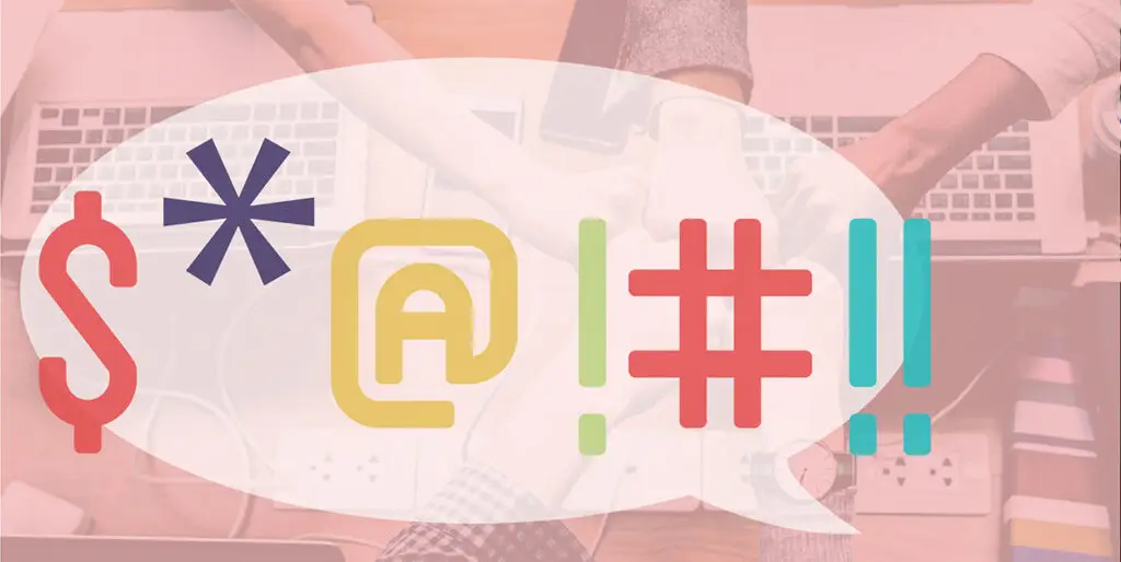 Coworkers fistbump over a table filled with laptops while a cartoon speech bubble indicates a swear word with symbols