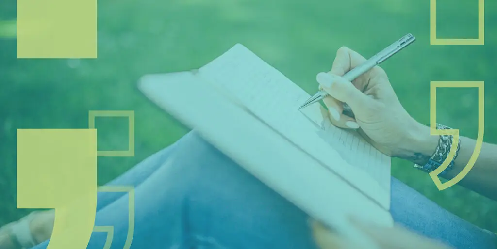 A person with blue painted nails writes in a notebook while relaxing outside