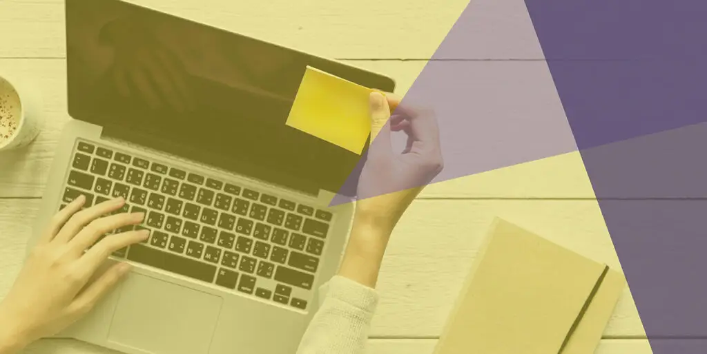 A person placing a sticky note on the corner of a laptop screen as a reminder