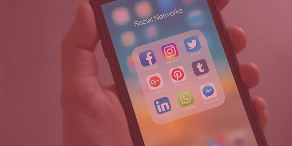 A man holds a cellphone that displays multiple social media icons, including Google+.