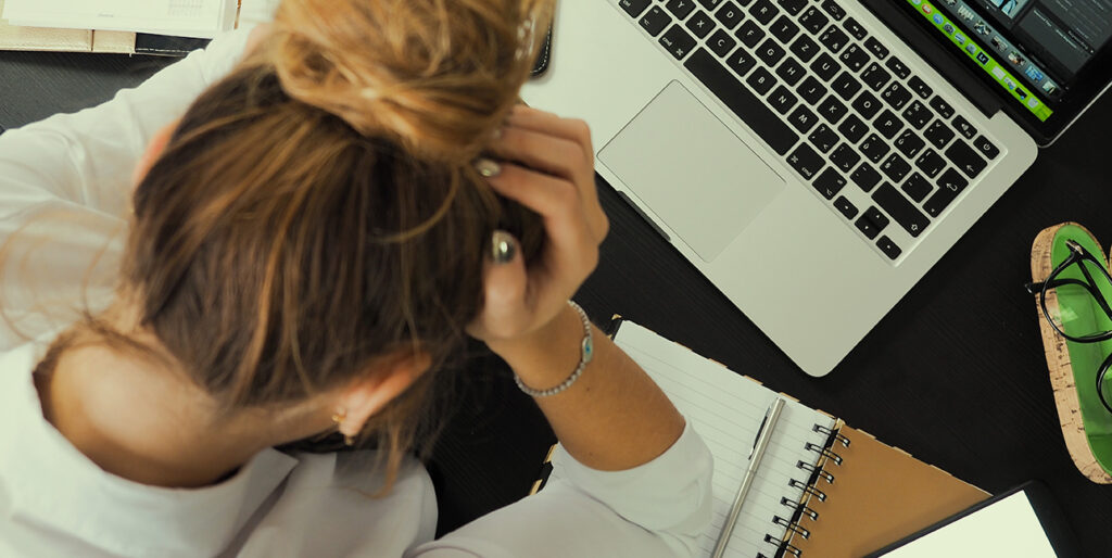 An employee sits with her head in her hands as she stares down at her laptop.