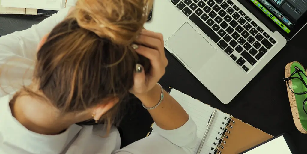 An employee sits with her head in her hands as she stares down at her laptop.