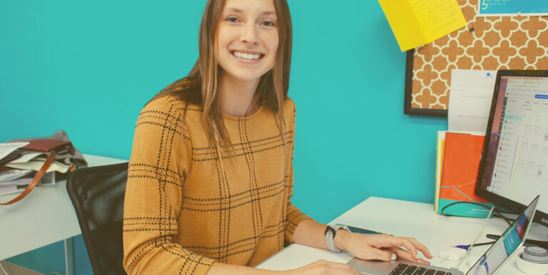 A photo of 8THIRTYFOUR's PR specialist, Bri Zimmer, smiling at her desk.