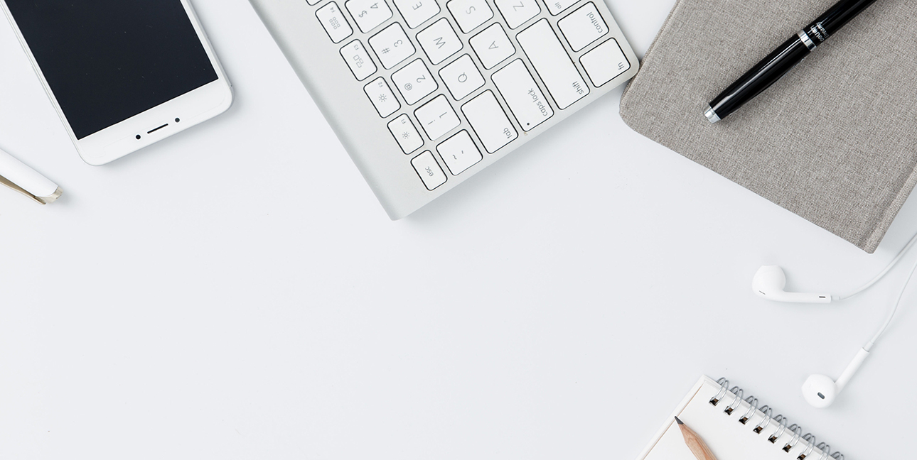 A flat lay of a keyboard, a phone, a journal and a pen.