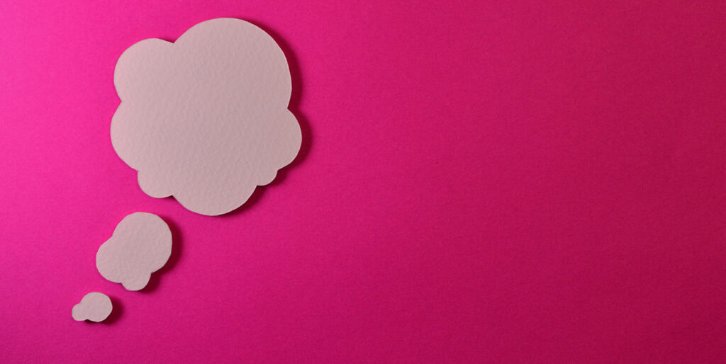 A cardboard cutout of a thought bubble arranged on top of a bright pink surface.