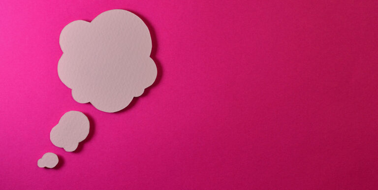 A cardboard cutout of a thought bubble arranged on top of a bright pink surface.