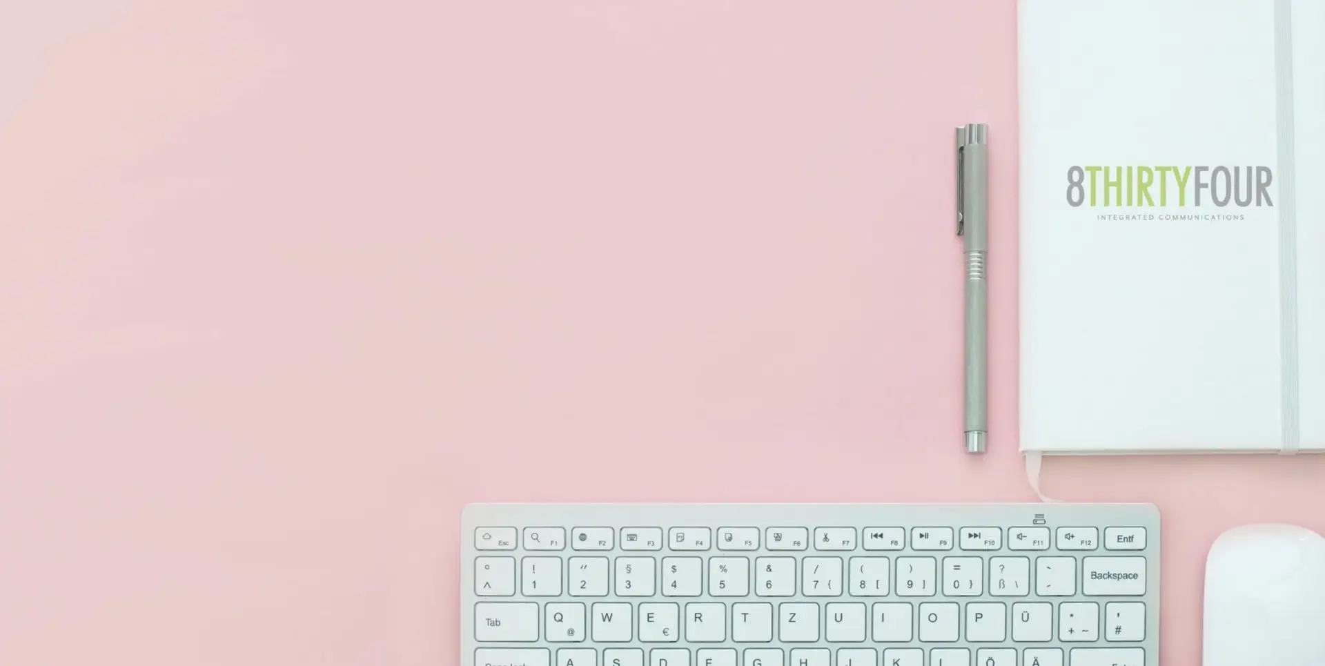 An image of a laptop, pen and journal against a pink table.