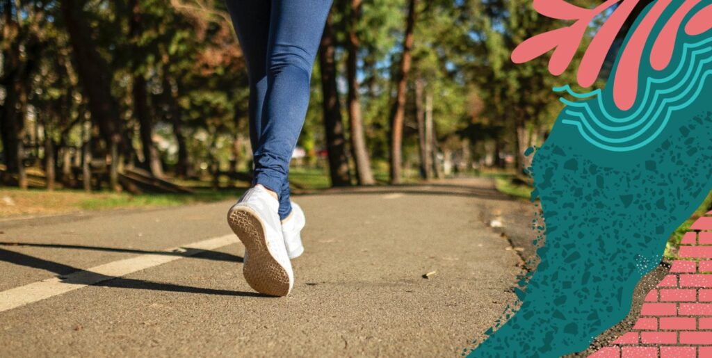 Someone in jeans and sneakers running down a paved and wooded trail.