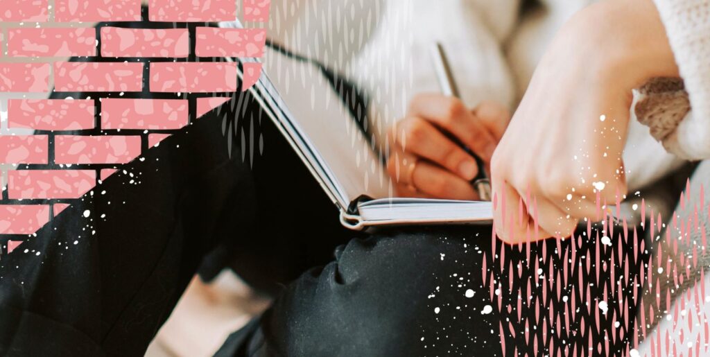 A person sitting against a wall, wearing jeans and a sweater, writing in a diary