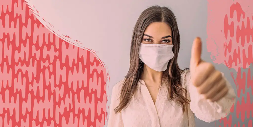 A woman wearing a mask and giving the camera a thumbs up.