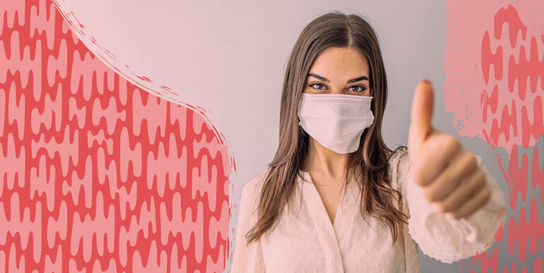 A woman wearing a mask and giving the camera a thumbs up.