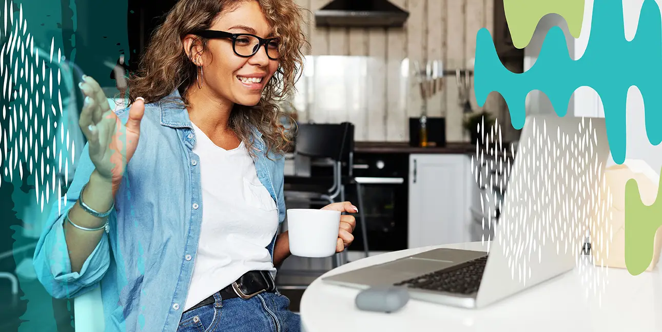 A woman holding a cup of coffee while working at her laptop