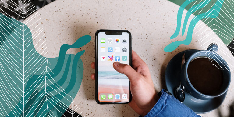 A person holding a smart phone sitting next to a cup of coffee.