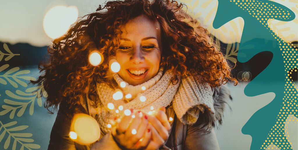 A woman smiling and holding string lights in her hands.