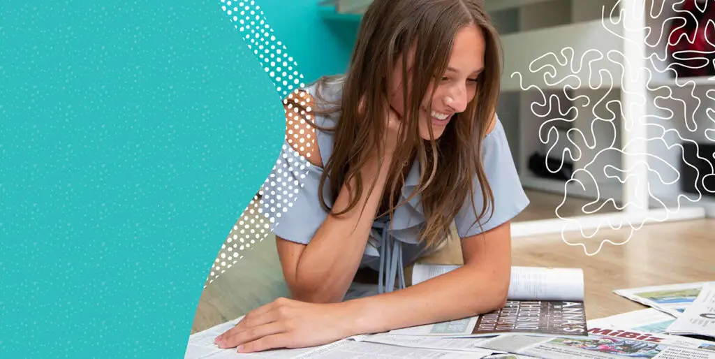 A woman smiling while reading the newspaper.