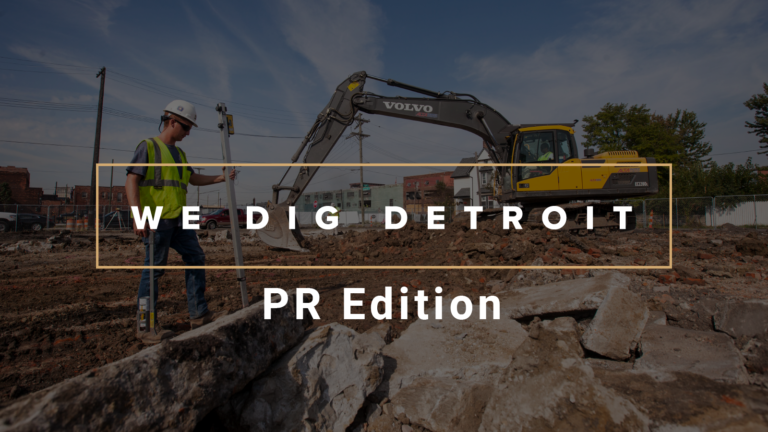 An excavator clearing dirt in front of the Detroit city skyline