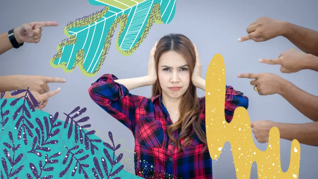 A woman covers her ears with her hands while several people point at her angrily.