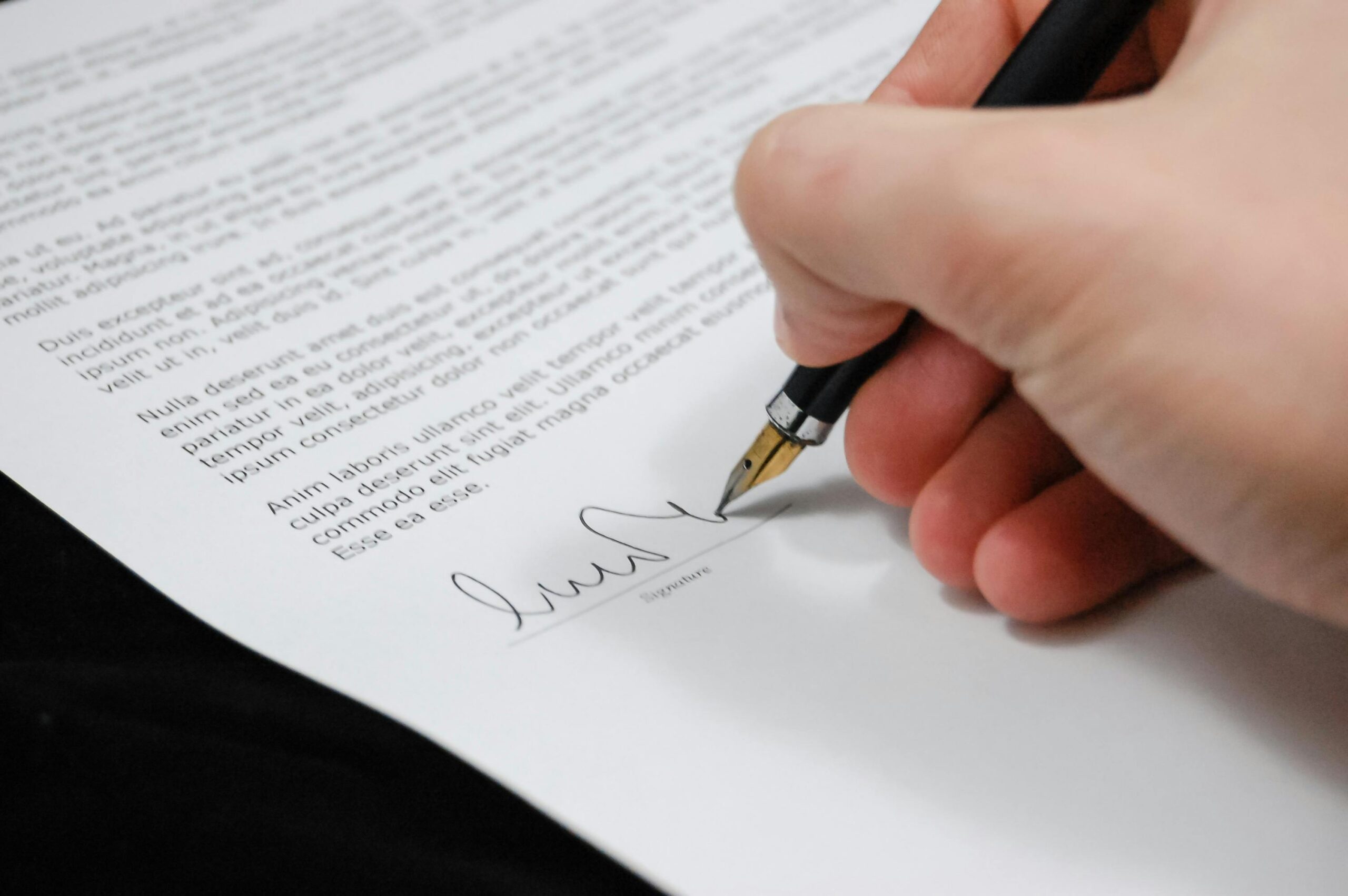 a close up of a man signing a document with a pen