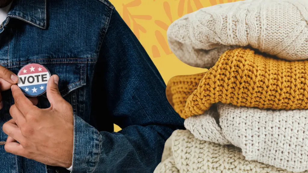 A person pins an "I voted" pin to their shirt next to a pile of sweaters