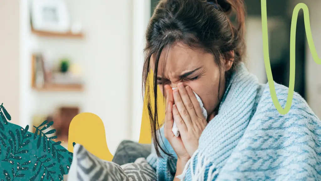 A woman covered in a blue blanket blows her nose.