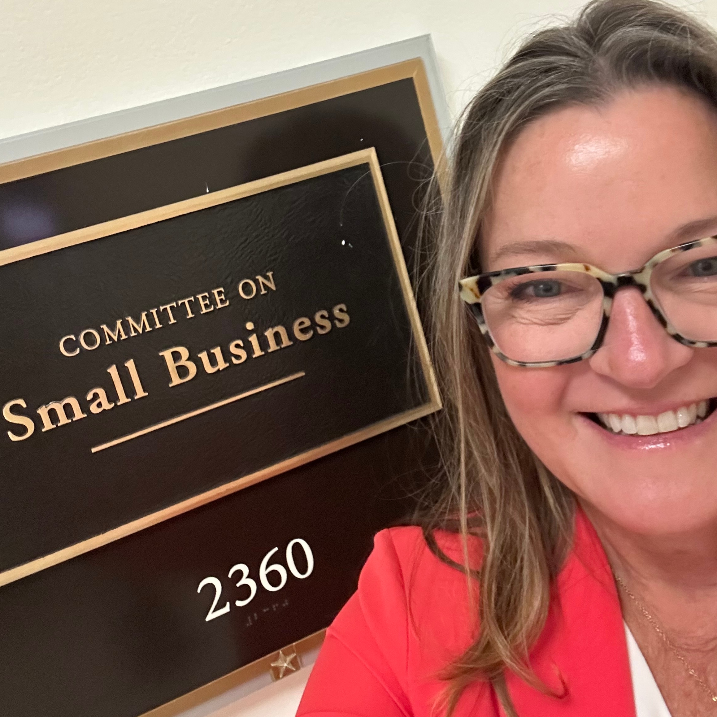 Sue Tellier poses by the sign for the Committee on Small Business
