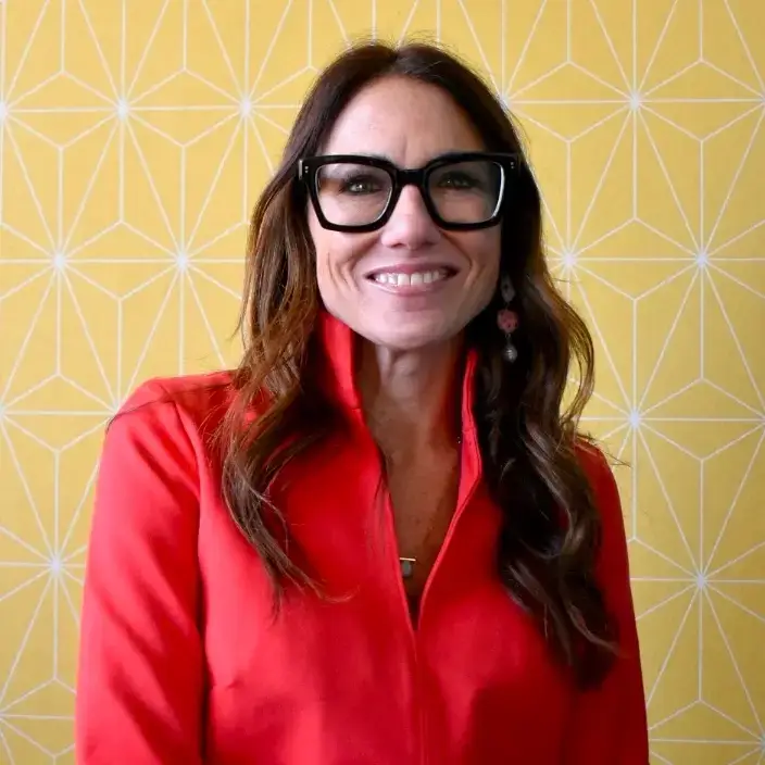 Kim Bode smiles while wearing a red jacket in the 8THIRTYFOUR office.