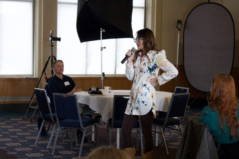 Kim stands at the front of a room. She's holding a microphone giving a speech to a room full of PR professionals.