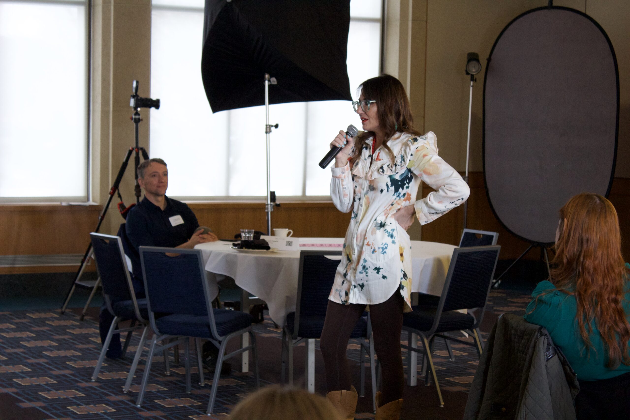 Kim stands at the front of a room. She's holding a microphone giving a speech to a room full of PR professionals.