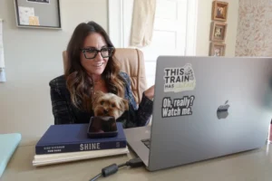 Kim Bode sits at her desk, laptop open while holding her dog. She smiles as she's on call.